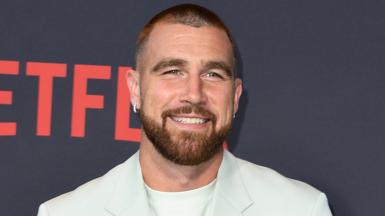 Travis Kelce smiling in an off-white suit
