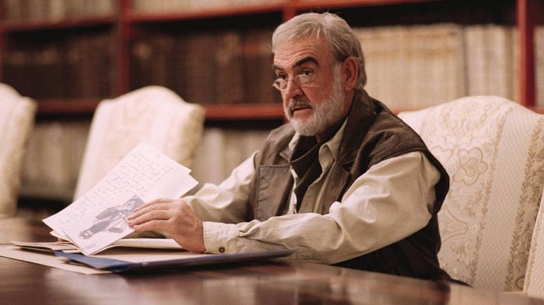 Quatermain sits at a table with papers