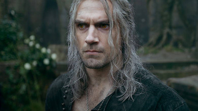 Geralt stands in the woods, scowling at something off-screen.