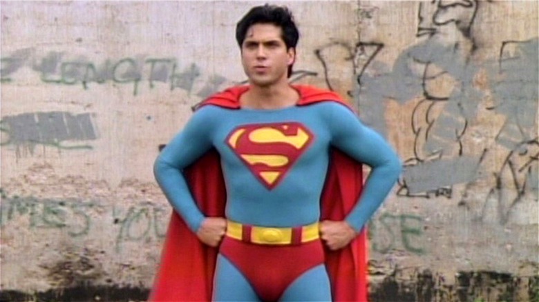 Superboy stands in front of a wall covered in grafitti, his hands on his hips.