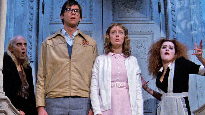 Brad and Janet standing at the front steps, flanked by Riff Raff and Magenta