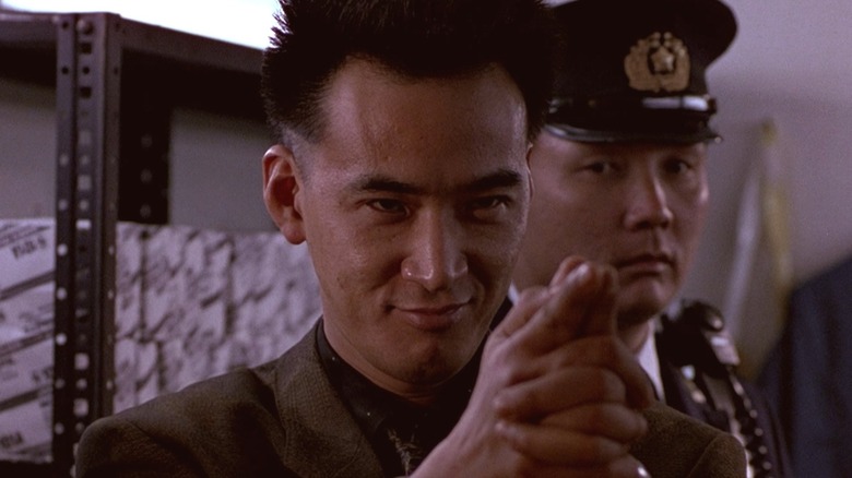 Koji Sato smiling while clasping his hands in "Black Rain" (1989)