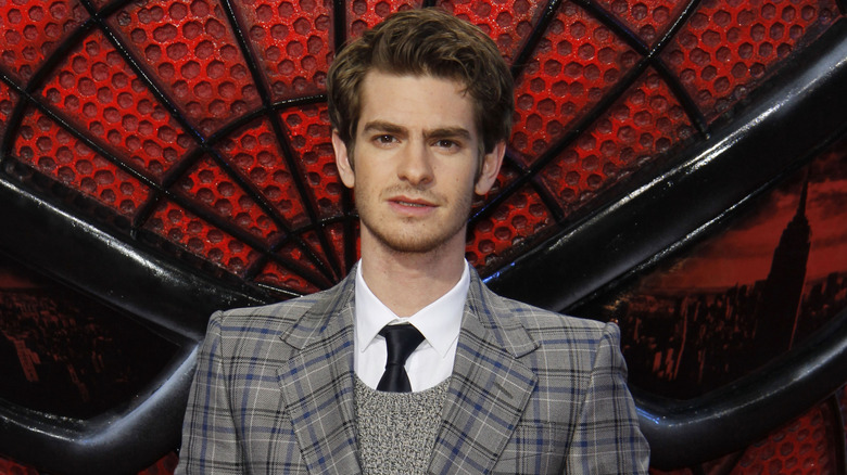 Andrew Garfield in front of a large Spider-Man mask logo