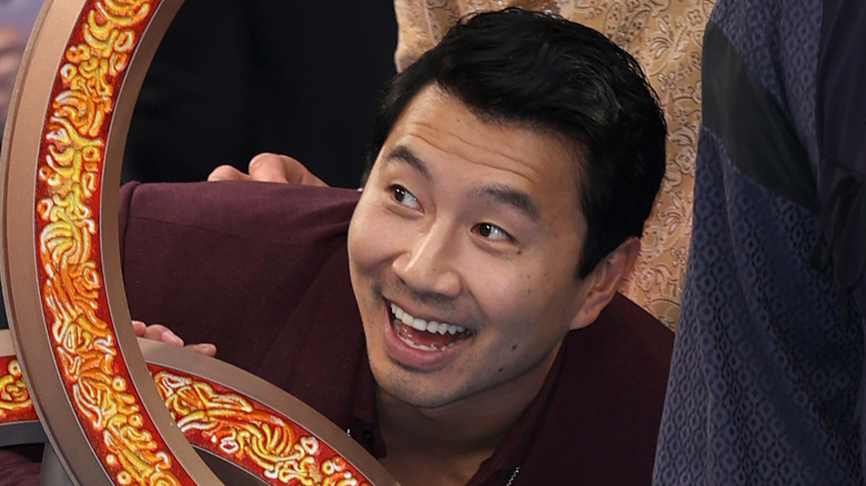 Simu Liu smiling behind a replica of the Ten Rings