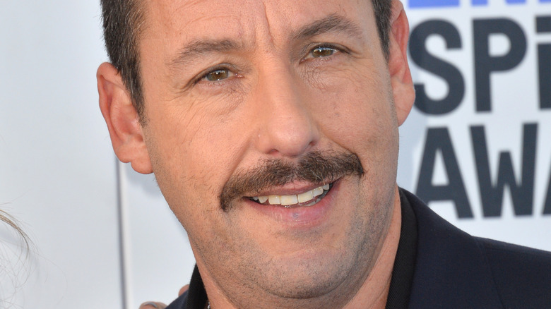 Adam Sandler smiling with a thin mustache