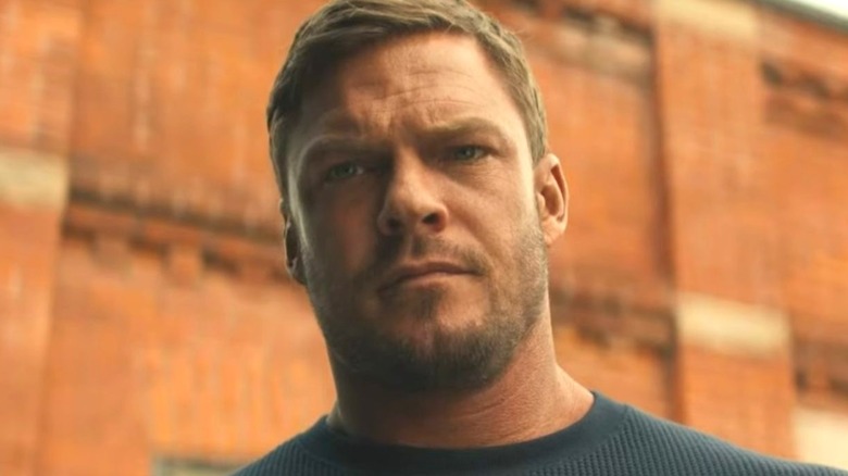 Reacher stands tall in front of an old brick building in "Reacher" (2022-present)
