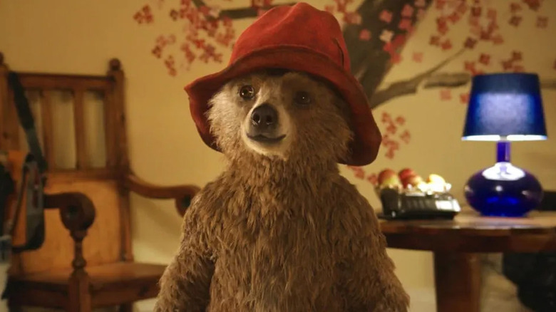 Paddington without a shirt on standing in the Brown house wearing his red hat in Paddington