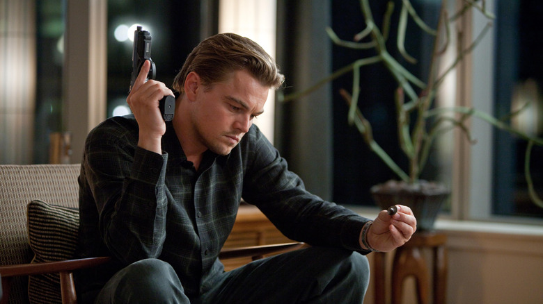 Don Cobb holding a pistol and a simple top, sitting in a chair, in Inception (2010)