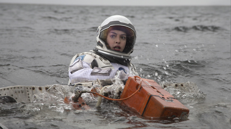Dr. Amelia brand struggling in the water in a space suit, holding an orange box, in Interstellar (2014)