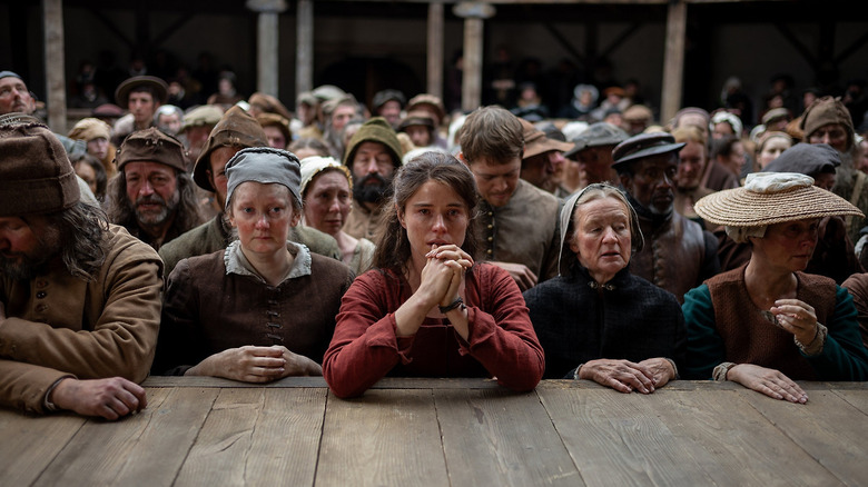 Agnes leans on the edge of the stage amid theatergoers in "Hamnet" (2025)