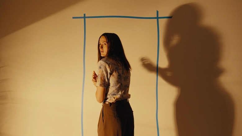 Mary standing in from of a wall with the outline of a door in Backrooms