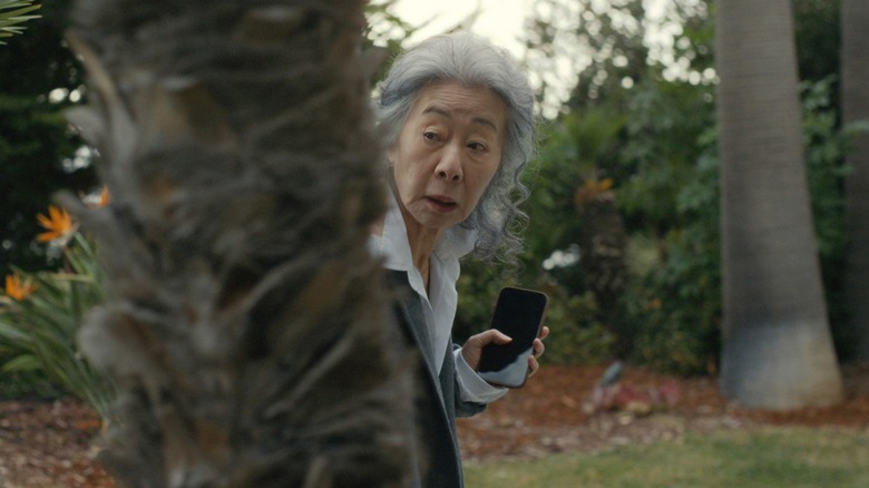 Chairwoman Park hiding behind a tree while holding cell phone in 