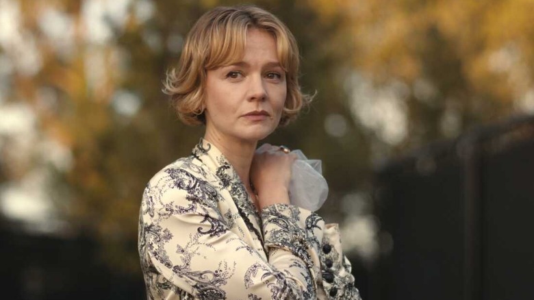 Lindsay, in a patterned off-white dress, holds something to her shoulder in "Beef"