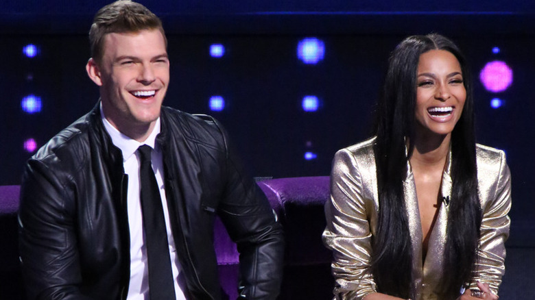 Alan Ritchson and Ciara smiling on a couch in "I Can Do That."