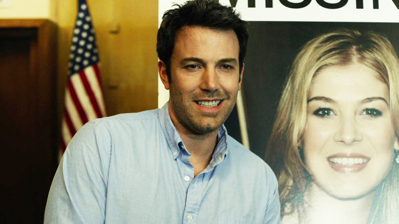 Nick Dunne smiling in front of a missing poster on Gone Girl