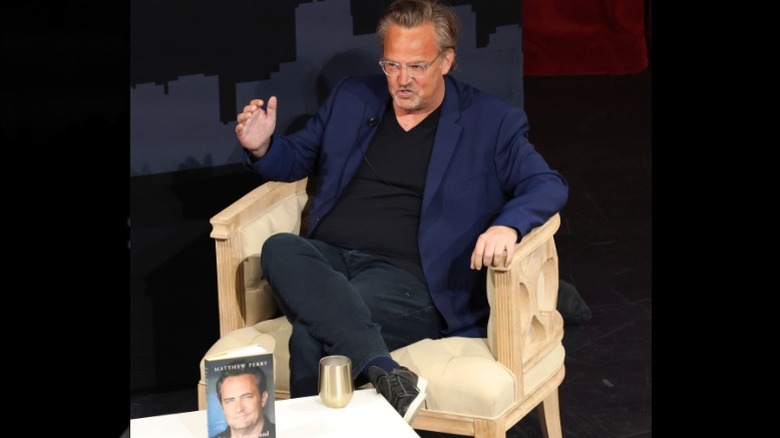 Matthew Perry sitting on a chair and gesturing