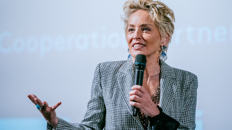 Sharon Stone in a grey suit holding a microphone