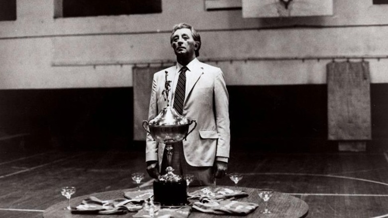 Coach Delaney standing somberly behind trophy in "That Championship Season" (1982)