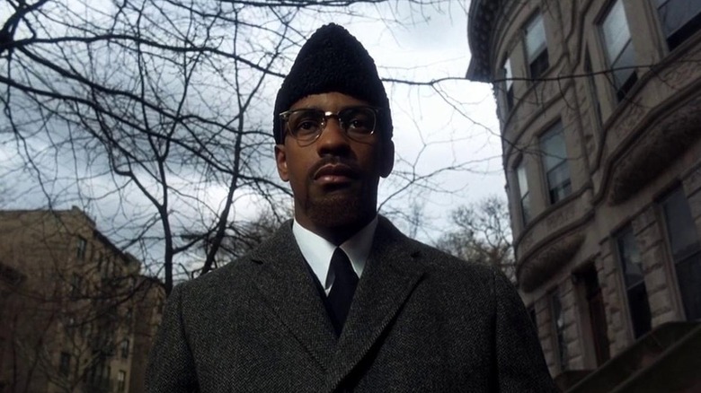 Malcolm X walking toward the camera in a winter coat and karakul hat