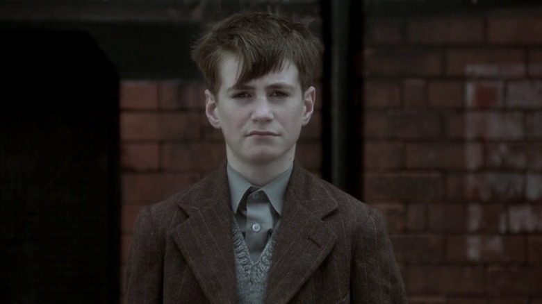 Bud standing with a brick wall behind him in The Long Day Closes