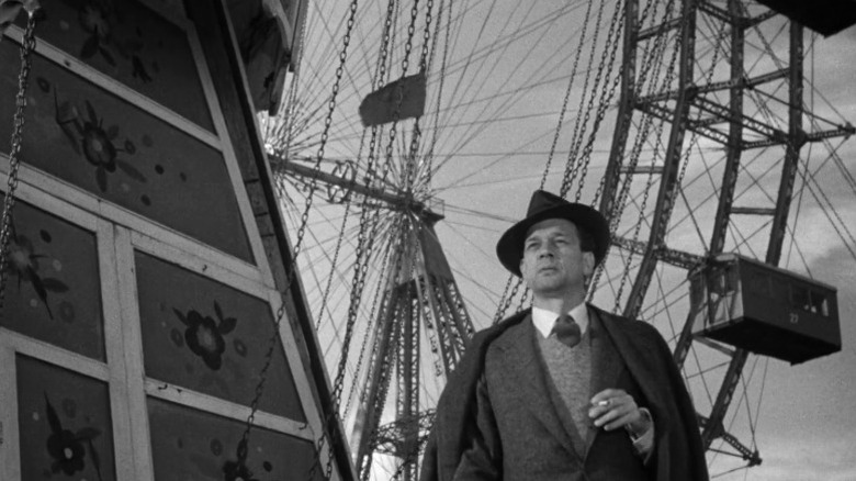 Holly standing next to a ferris wheel with a cigarette in his hand in The Third Man