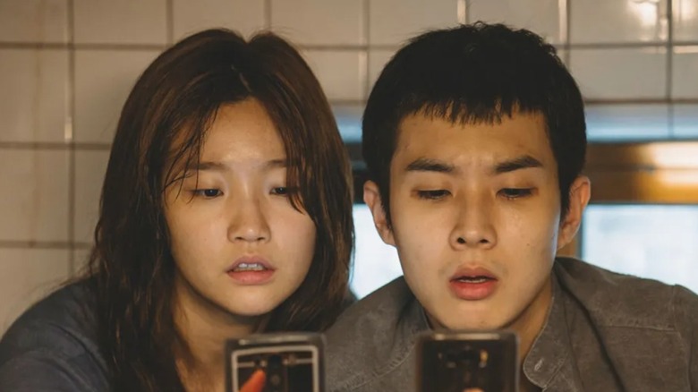 Ki-Jung and Ki-woo look at their phones in the bathroom in Parasite (2019)