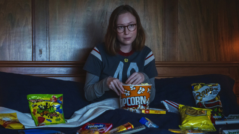 Kris eating junk food in bed in "Teenage Sex and Death at Camp Miasma" (2026)