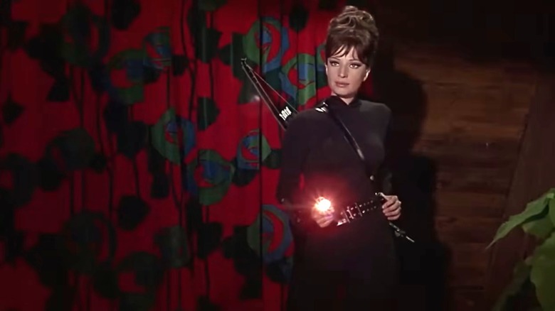 Modesty Blaise stands holding a flashlight in "Modesty Blaise" (1966)