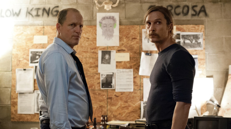 Marty and Rust looking at something with a wall of evidence behind them on True Detective
