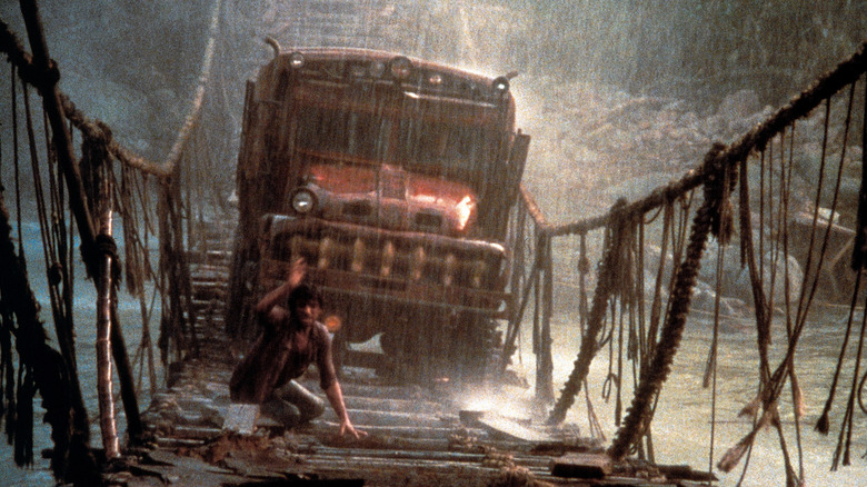 Truck driving on rope bridge with man in front