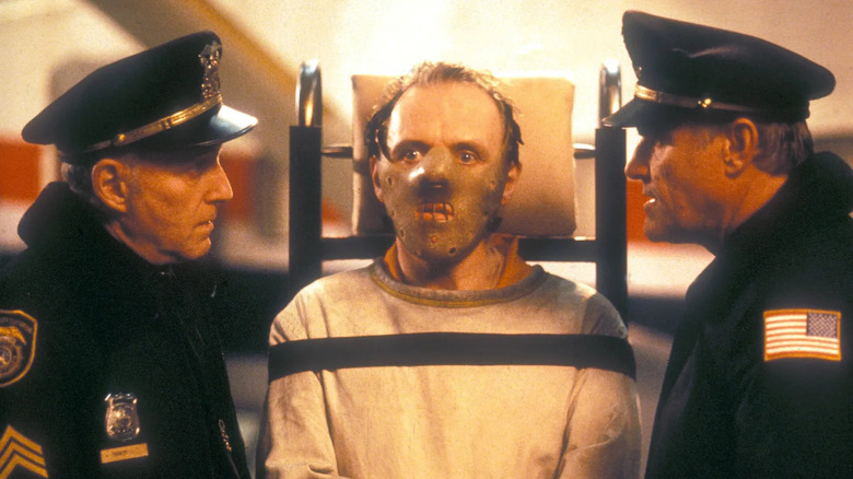 Hannibal Lecter in a straitjacket and mask, flanked by cops