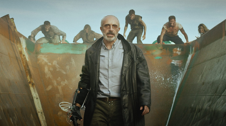A man in a trench coat stands in a metal container as other people advance behind him in "Silent Zone"