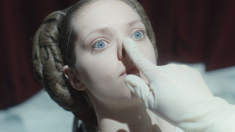 A gloved hand holds a finger against Elvira's nose in "The Ugly Stepsister"