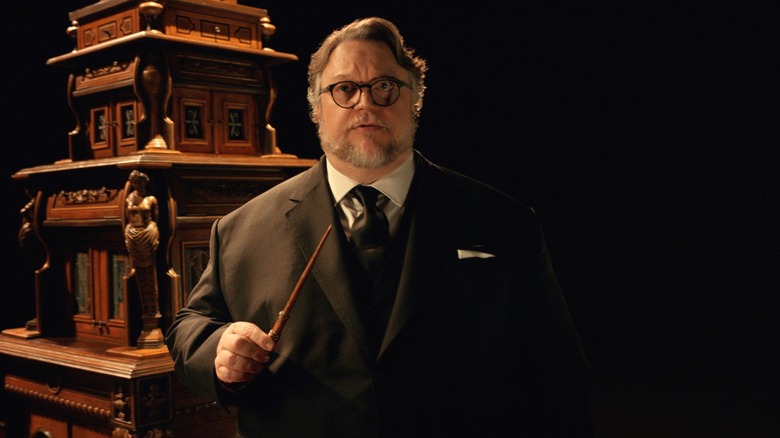Guillermo del Toro holding a wand and standing in front of a cabinet in "Cabinet of Curiosities."