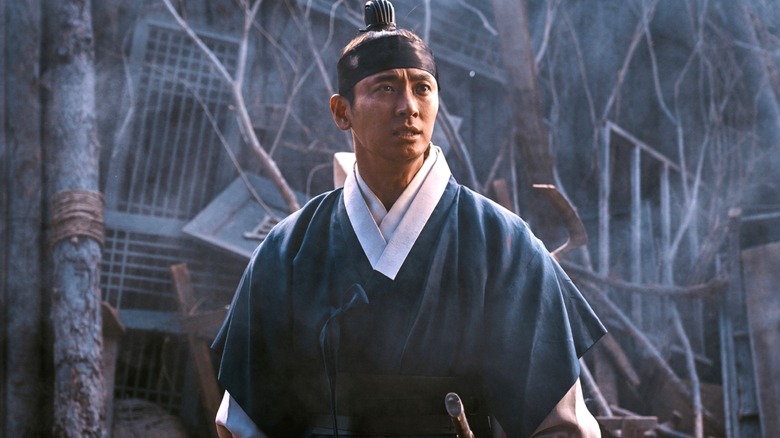 Lee Chang standing in front of a destroyed building in "Kingdom" Season 2.