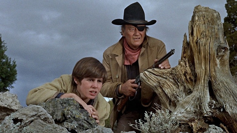 Rooster Cogburn crouched on rocks with Mattie in "True Grit" (1969)