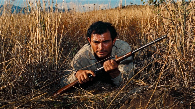 Alfonso Parral lying in a field while holding a gun in "The Bravados"