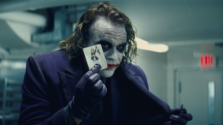 The Joker holds a Joker playing card while wearing a purple suit in "The Dark Knight"