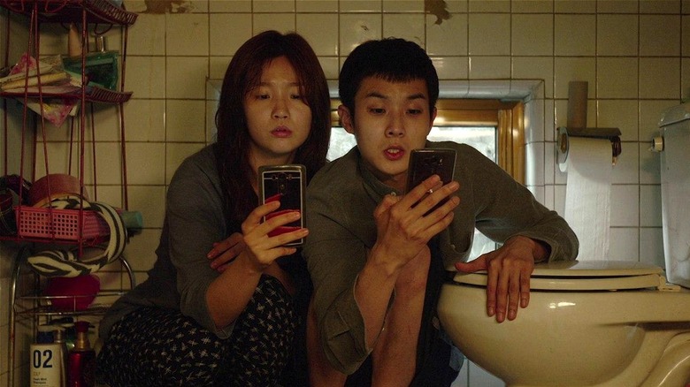 Ki-jung and Ki-woo using their phones by the toilet in Parasite (2019)