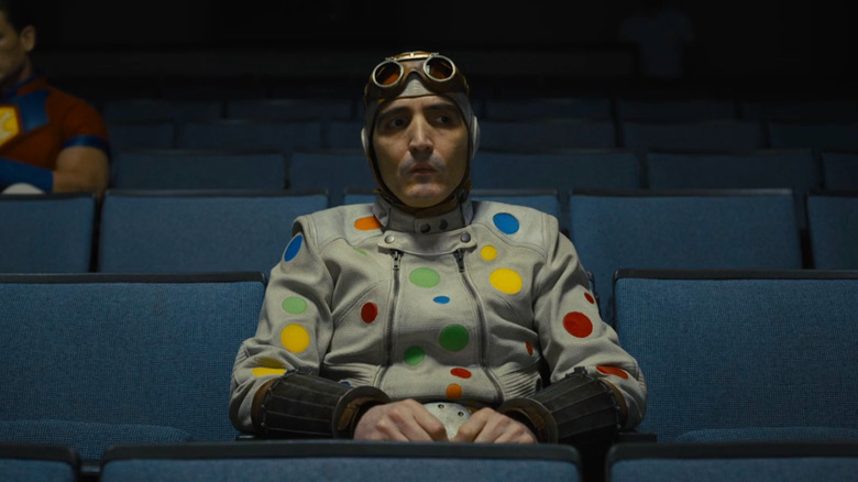 Polka-Dot Man sitting in an auditorium with Peacemaker in the background in 