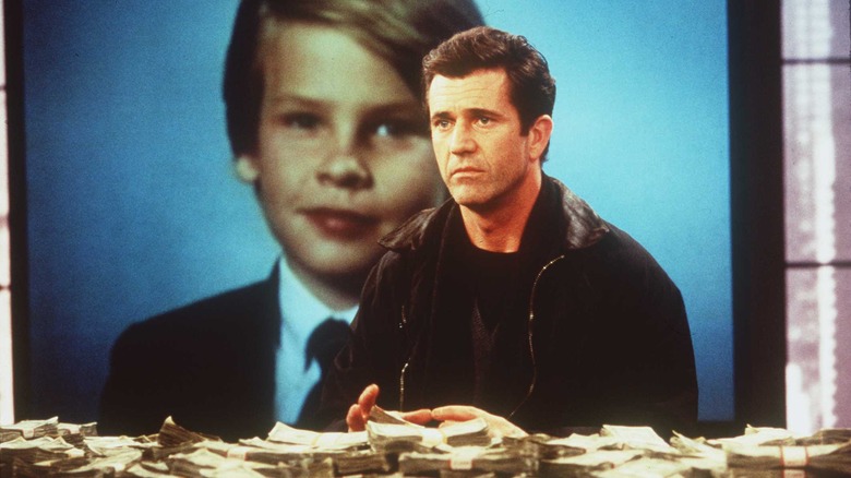 Tom sits in front of a pile of cash with his son's photo behind him in "Ransom" (1996)