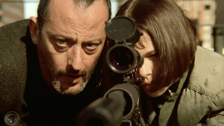 Léon helps Mathilda aim through the scope of a rifle in Léon: The Professional