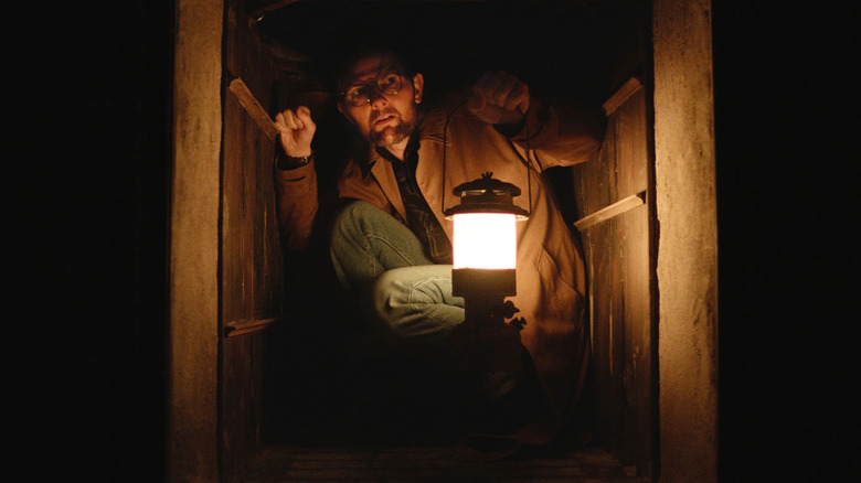 Ohm crouching in a dumbwaiter with a lantern in Hokum