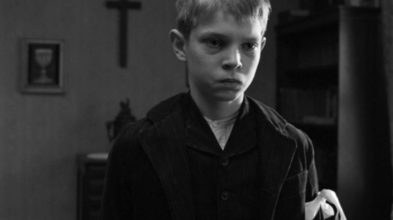 a solemn boy with white ribbon on arm
