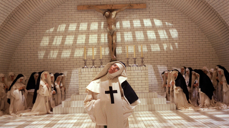 Sister Jeanne tilting head while nuns pray behind her