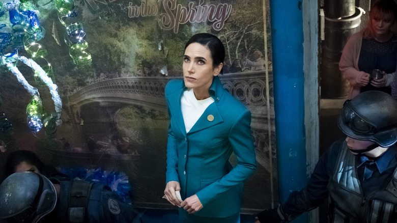 Melanie looks up, wearing a blue suit and flanked by guards in Snowpiercer (2020)