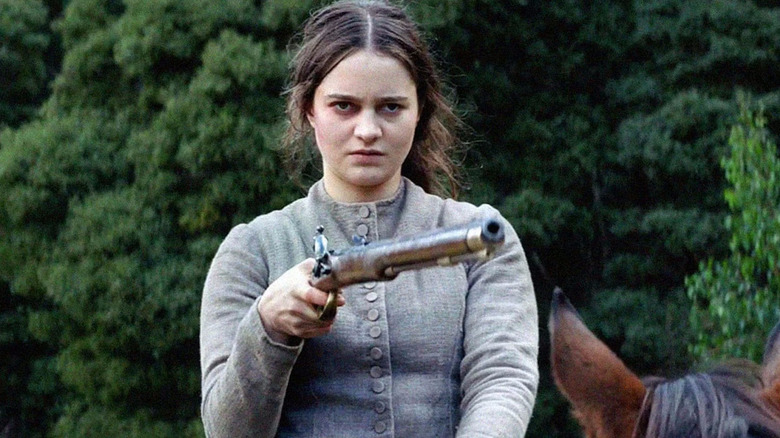 Clare Carroll in a modest dress holding a long gun in The Nightingale