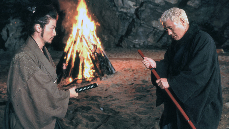 Zatoichi and Genosuke drawing weapons by a fire (2003)