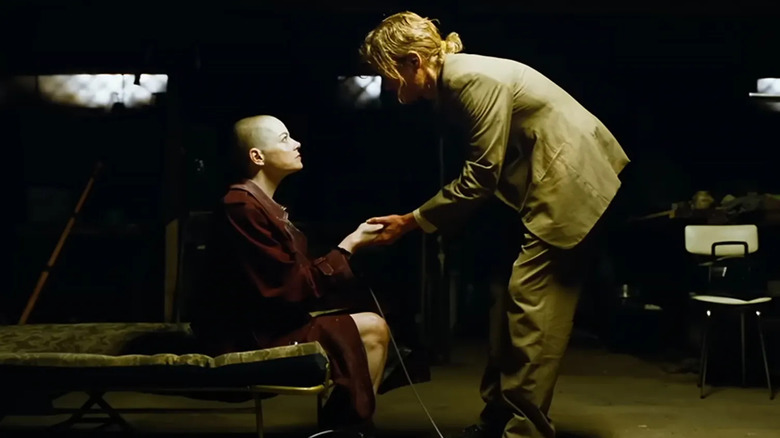 Teddy Gantz stands over bald Michelle Fuller in a dark basement in "Bugonia" (2025)