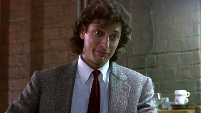 Seth Brundle wears a tweed blazer with a red tie in 